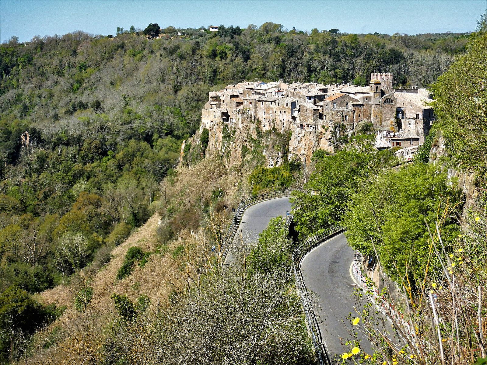 Calcata vista da lontano: le case del borgo antico sulla rupe di tufo, con la strada che sale tra i boschi