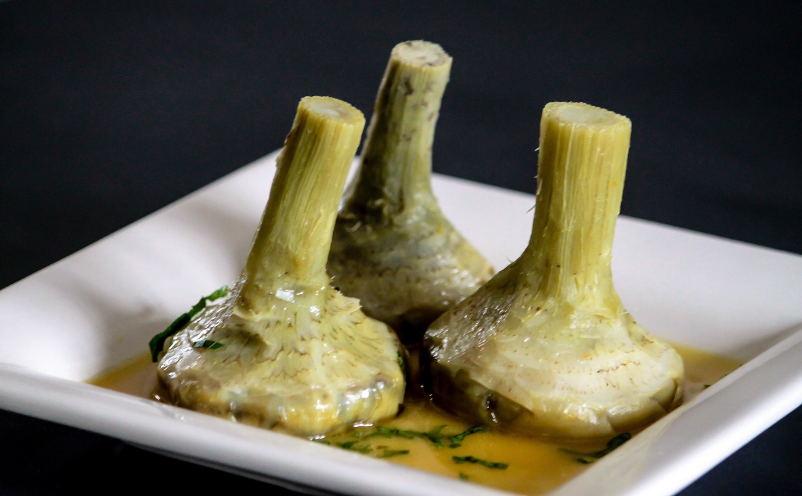 Tre carciofi alla romana in piedi sul piatto, con il gambo, nel loro olio con la mentuccia
