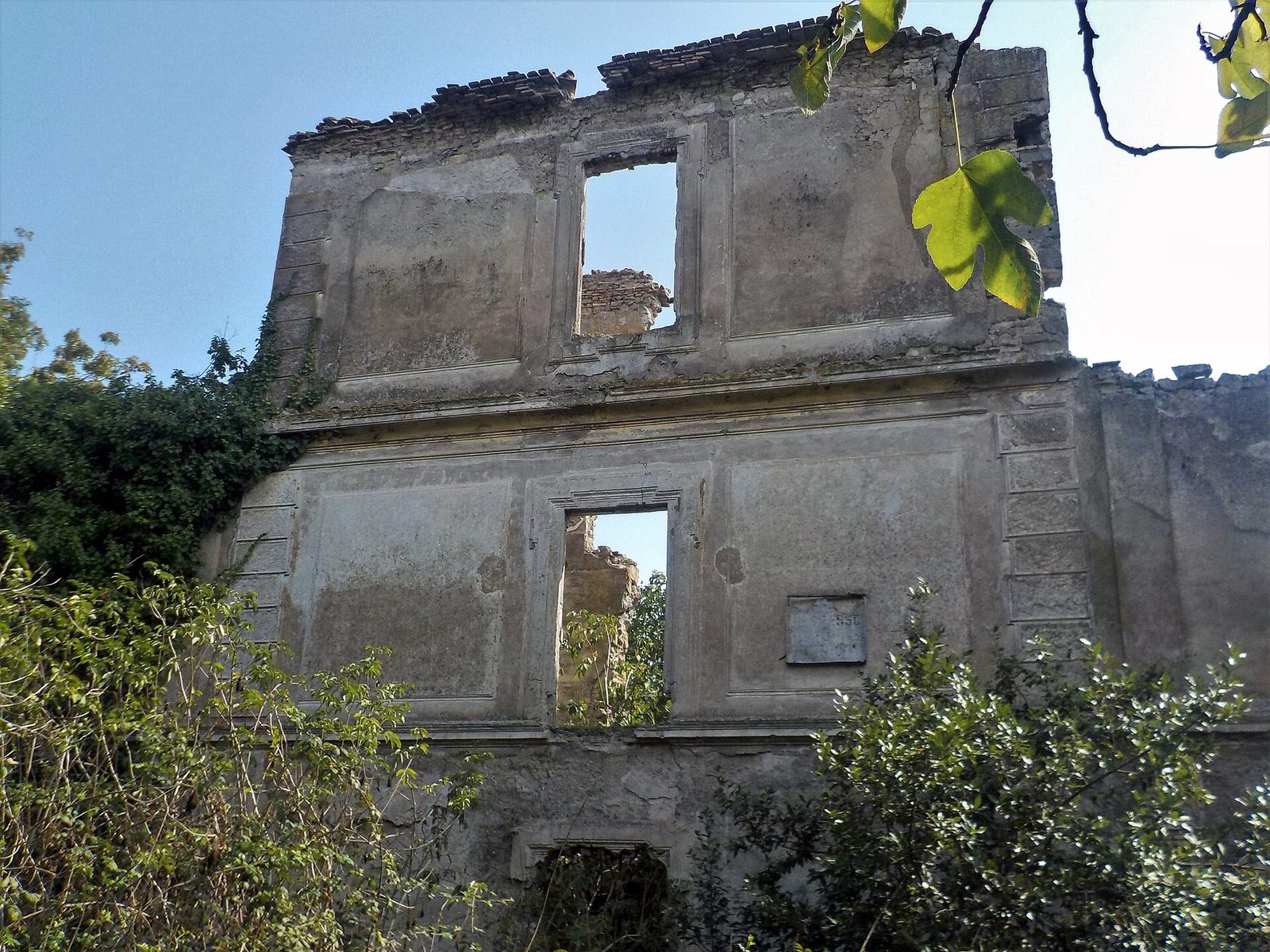 Muri in rovina di Villa Chigi Versaglia a Formello, con finestre aperte sul cielo e vegetazione